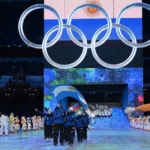 Delegación argentina con la bandera nacional bajo los aros olímpicos durante un desfile de ceremonia.