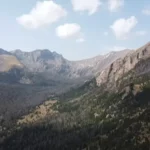 Vista aérea de un valle montañoso con bosque y cielo parcialmente nublado